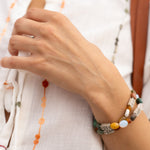 Close-up of a hand wearing a colorful beaded bracelet on a light background