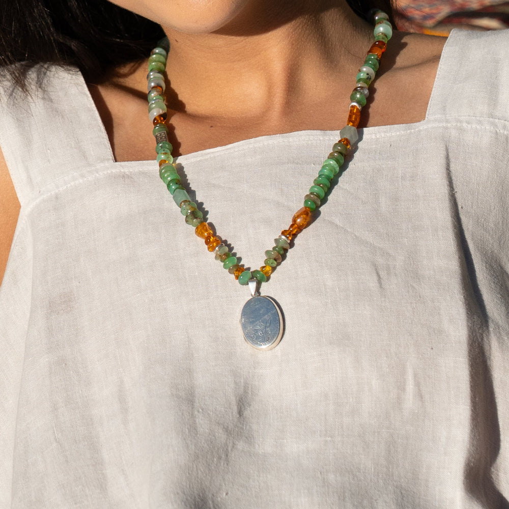 Necklace with green and orange beads and a silver pendant on a white background