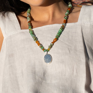 Necklace with green and orange beads and a silver pendant on a white background