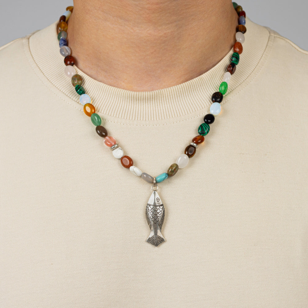 Necklace with a fish pendant worn by a person on a plain background