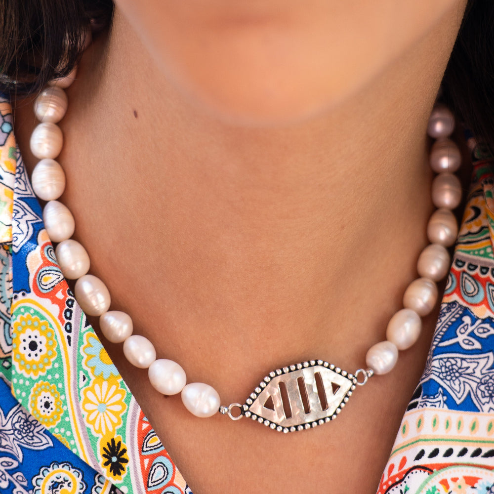 Pearl necklace with a silver clasp worn by a person against a colorful patterned background