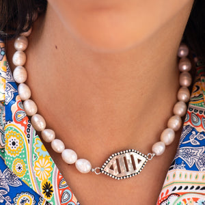 Pearl necklace with a silver clasp worn by a person against a colorful patterned background