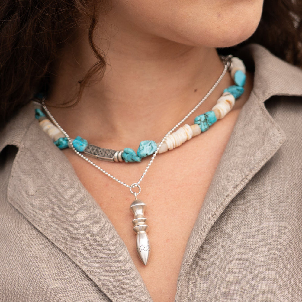Necklace with turquoise and white beads and a silver pendant worn by a person.