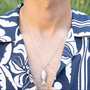 Man wearing a blue and white patterned shirt with a necklace featuring a fish pendant.