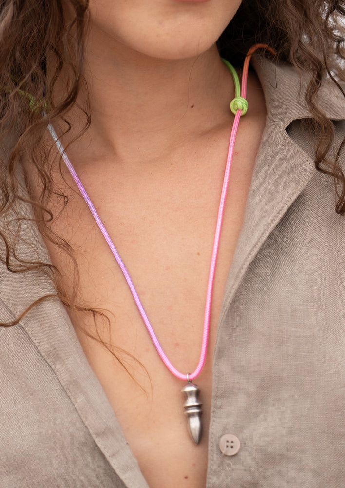 Necklace with a pink cord and silver pendant worn by a person